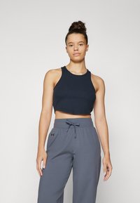 Tamno plavi rebrasti crop top i sive široke atletske hlače s podesivim pojasom i logotipom sa strane. Glatka tekstura.