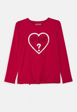 Chemise rouge à manches longues avec contour de cœur argenté à l'avant et logo "GUESS", avec un point d'interrogation et un détail de nœud à l'ourlet.