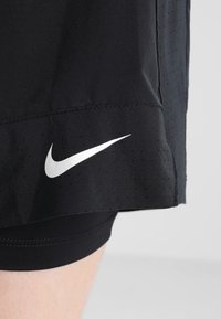 Pantalones cortos deportivos negros hechos de tela ligera con textura perforada. Presentan el logo blanco de Nike en forma de “swoosh” en la parte inferior izquierda.