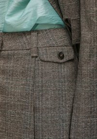Grijze geruite pak met een gestructureerde stof, voorzien van een getailleerde pasvorm, zijzak en een donkere knopenaccent. Gelaagd over een lichtblauw top.