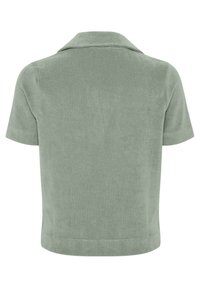 Top vert clair à manches courtes avec un large col, vu de dos, en tissu doux et texturé avec un ourlet droit.