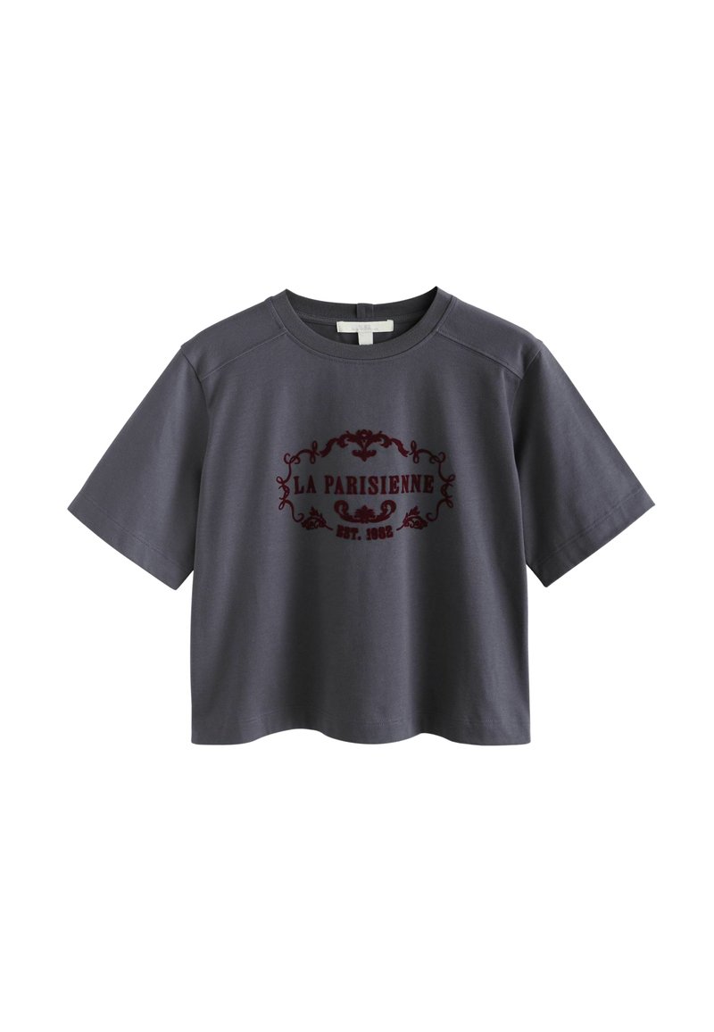 Graues, kurzärmliges, cropped T-Shirt aus Baumwolle mit rundem Halsausschnitt, das ein burgunderrotes Druckdesign mit dem Text "LA PARISIENNE EST. 1982." zeigt.