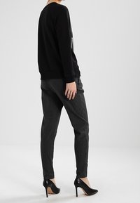 Felpa nera con polsini a coste, abbinata a pantaloni grigi a righe sottili. Il modello indossa scarpe con tacco nere. Silhouette semplice e moderna.