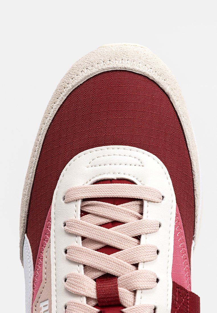 Baskets rouges et beiges avec textures en tissu et en daim, dotées de lacets crème, d'une languette blanche et d'un capuchon de protection renforcé. Détails de rayures horizontales.