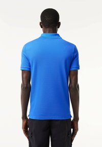 Polo de manga corta en azul brillante, hecho de una tela texturizada. Presenta un color clásico y una abertura lateral en el dobladillo.