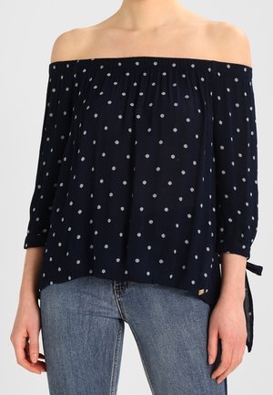 Blusa navy off-the-shoulder con pois bianchi, scollo arricciato, maniche a tre quarti e legature laterali, realizzata in tessuto leggero.