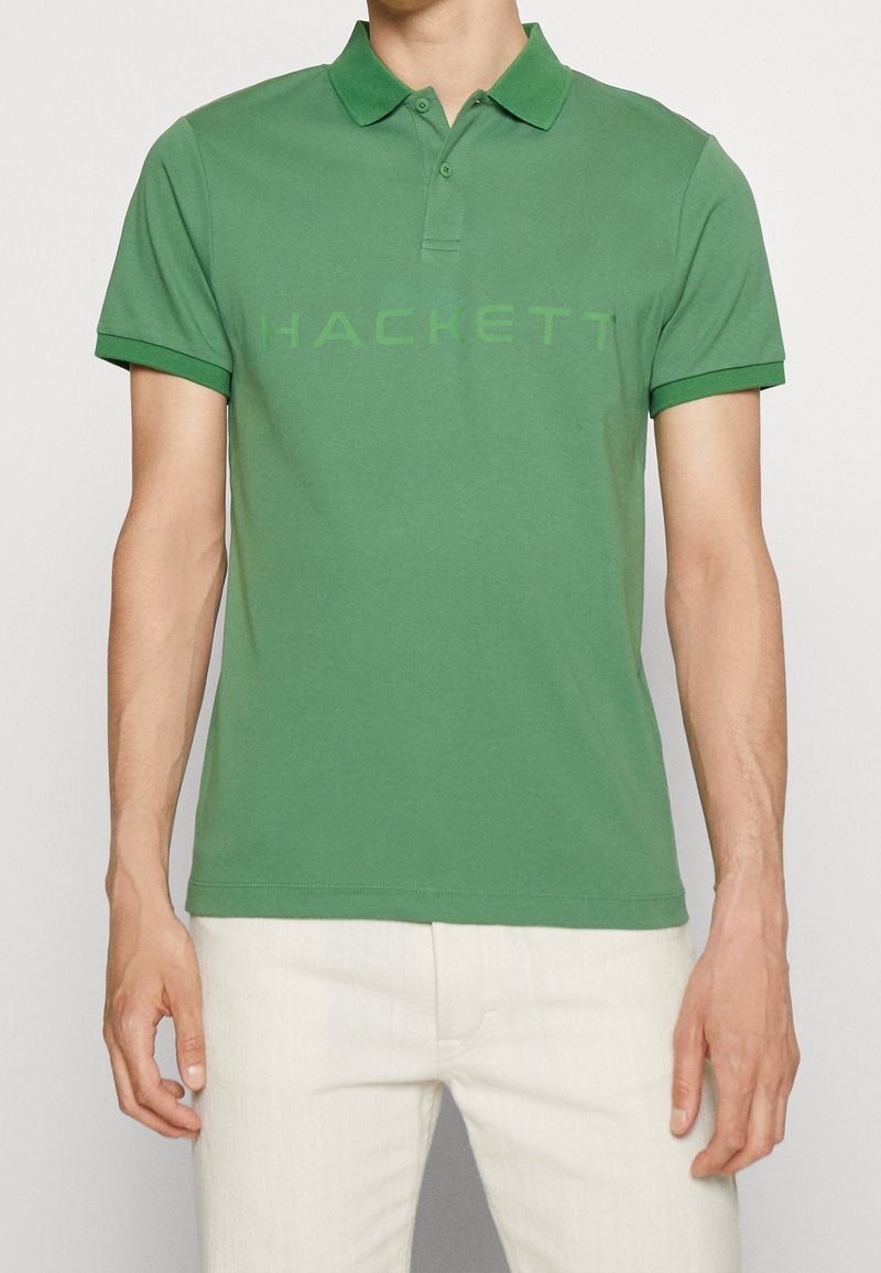 Polo en coton vert avec un col classique, des manches courtes et le mot "HACKETT" imprimé en vert clair sur le devant.