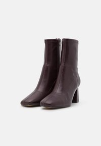 Bottes chevilles en cuir bordeaux avec un bout carré, un talon bloc haut, une fermeture éclair latérale et un détail de couture distinctif le long des bords.