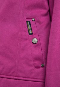 Fuchsia jacka med en slät yta, utrustad med en ficka i lapptäckesteknik, metallknappslutning och en varumärkesetikett som är sydd på sidan.