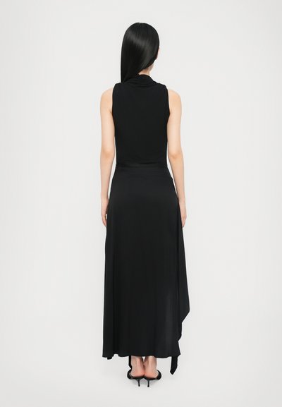 Black sleeveless dress with a cowl neck, floor-length design, flowing fabric, and asymmetrical hem. Worn with black high-heeled shoes.
