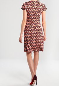 Krátké šaty s rukávem v červeném a černém geometrickém vzoru, přiléhavý pas, do délky kolen, s hladkou texturou a zaobleným lemem.