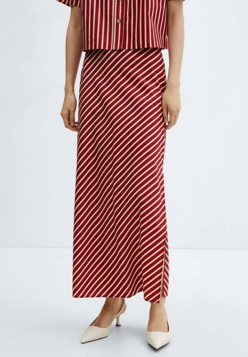 Femme portant une jupe maxi rayée rouge et blanche en diagonale avec une fente, associée à des talons blancs pointus et une chemise rayée rouge.