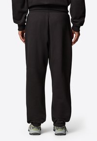 Czarne joggery z elastycznymi mankietami, wykonane z miękkiej bawełny, o luźnym kroju i pasku ze sznurkiem. W połączeniu z szarymi trampkami.