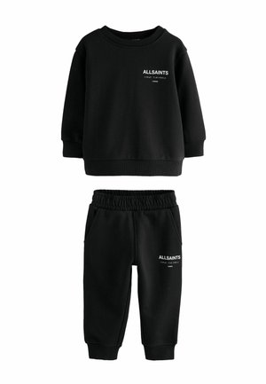 Mustat pitkät hihat -huppari ja jogginghousut, jossa valkoinen "ALLSAINTS LONDON" -teksti ja japanilaisia merkkejä molemmissa osissa.