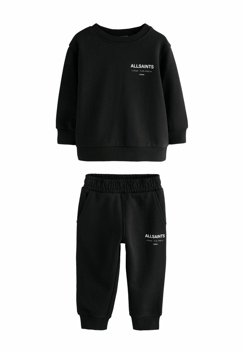 Mustat pitkät hihat -huppari ja jogginghousut, jossa valkoinen "ALLSAINTS LONDON" -teksti ja japanilaisia merkkejä molemmissa osissa.