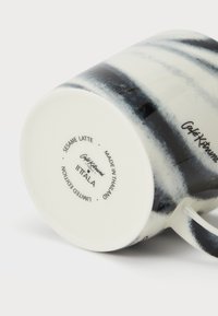 Taza de cerámica para latte en blanco con patrón de pinceladas negras. Cuenta con un asa curva, base marcada con "Iittala" y la inscripción "Edición Limitada".