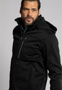 Schwarze Softshell-Jacke mit Kapuze, ausgestattet mit Reißverschluss-Taschen und kontrastierenden Akzenten. Der Stoff wirkt glatt und dehnbar.
