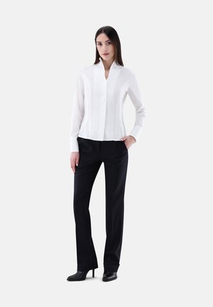 Weißes Langarmbluse mit V-Ausschnitt, mit einer glatten Textur. Kombiniert mit schwarzen maßgeschneiderten Hosen und schwarzen High Heels.