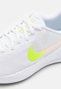 Bílé texturované sportovní boty s neonově zeleným logem Nike, bílými tkaničkami a hladkou gumovou podrážkou; mají síťované boční panely.