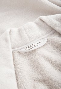 Weißer Bademantel aus Frottee mit einer weichen, strukturierten Oberfläche und einem Etikett mit der Aufschrift "FÉRAUD PARIS" am Kragen.