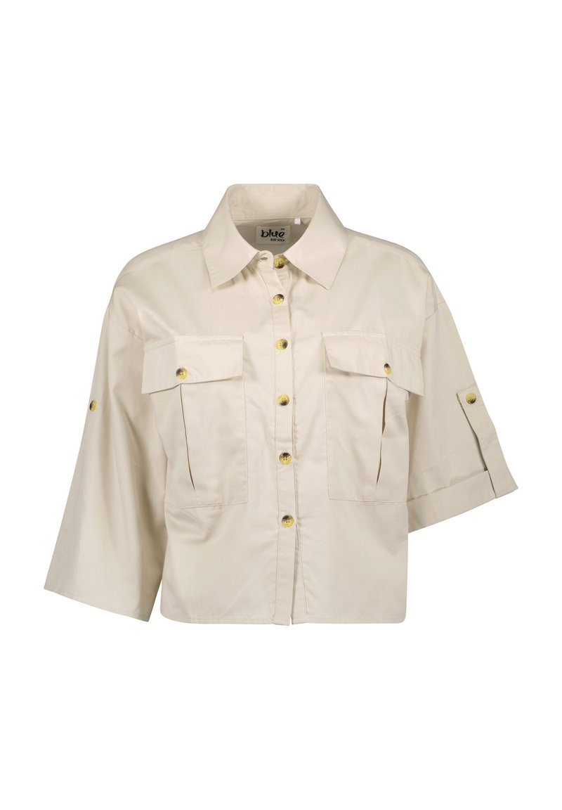 Camicia beige accorciata con colletto strutturato, due tasche sul petto e maniche corte. Caratterizzata da bottoni gialli e un tessuto liscio e leggero.