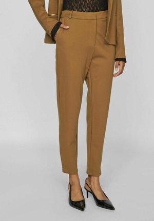 Brązowe spodnie w klasycznym kroju z gładkiego, sztywnego materiału mają średni stan i tapered nogawkę. Połączone z czarnymi szpilkami.