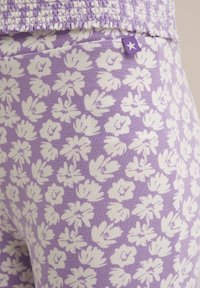 Lila leggings med ett vitt blommönster, tillverkade av mjuk, texturerad tyg. Har en liten lila etikett med stjärndesign.