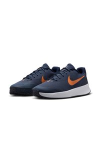 Baskets de sport bleu marine avec une tige en tissu texturé, logo swoosh orange et semelle en caoutchouc blanche. Conçues pour le confort et le soutien.