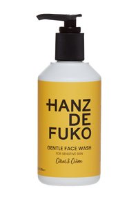 Nettoyant doux pour le visage dans une bouteille cylindrique blanche avec une étiquette jaune. Capuchon à pompe noir. Texte : "Hanz de Fuko, Citrus & Crème, pour peau sensible."