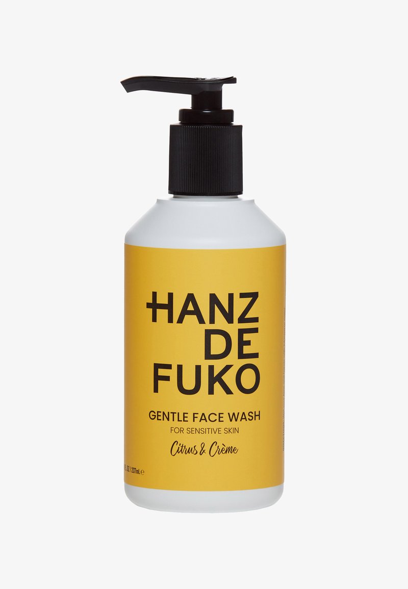 Zachte gezichtswash in een cilindervormige witte fles met gele label. Zwarte pompdeksel. Tekst: "Hanz de Fuko, Citrus & Crème, voor gevoelige huid."
