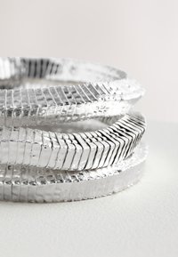 Stacked metallic rings with a textured surface, featuring a polished silver finish and a pattern of grooves throughout.