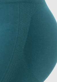 Close-up van teal rekbare stof, die het textuurpatroon en de contouren laat zien, waarschijnlijk van een stuk sportkleding of shapewear.