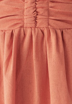 Kortsutatud korallivärvi kangas tekstuurse pinnaga. Materjal on pehme, sisaldades ülaservas kortsud ja allosas voolavaid voldikuid.