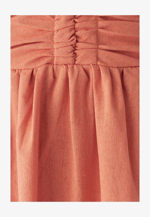 Marszczony koralowy materiał o teksturowanej powierzchni. Materiał jest miękki, z marszczeniami u góry i płynnymi plisami poniżej.