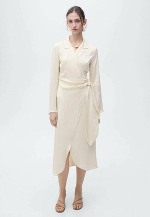 Cream wrap dress with long sleeves, soft fabric, a tied detail at the waist, and a front slit. Simple design, suitable for casual wear.