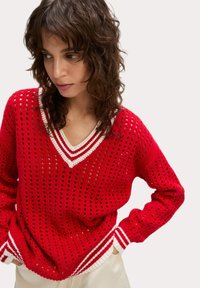 Roter Pullover aus Strick mit V-Ausschnitt und offenem Maschenmuster. Weiß gestreifte Akzente am Kragen und an den Bündchen. Lange Ärmel, lässige Passform.