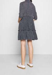 Marinblå lagad klänning med vita prickar, långa ärmar och krage; tillsammans med vita sneakers med gummisulor och röda detaljer.