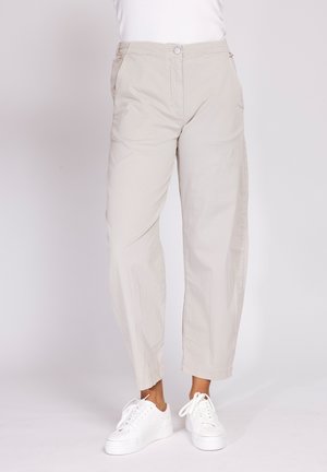 Person wearing beige ankle-length pants and white sneakers standing on a plain background.