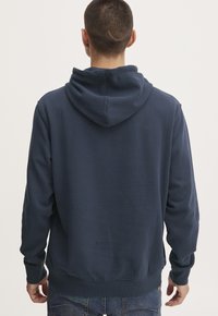 Sudadera azul marino con un ajuste relajado, capucha con cordón y puños acanalados. La tela parece suave, con un acabado liso y un detalle mínimo.
