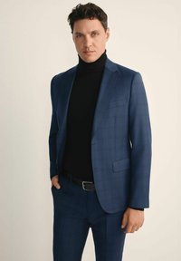 Niebieska marynarka w kratę założona na czarny golf, zaprezentowana w prostym kroju z eleganckimi klapami. Materiał wydaje się gładki z delikatną teksturą.