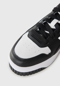 Black and white sneaker with a leather upper, textured accents, perforated toe box, and flat black laces on a white rubber sole.