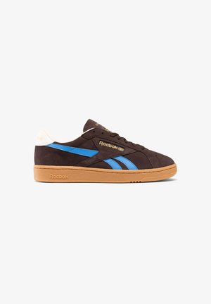 Zapatilla Reebok baja con ante marrón oscuro, rayas laterales azules, suela de goma, lengüeta trasera blanca y logotipos dorados de Reebok en el lateral y la lengüeta.