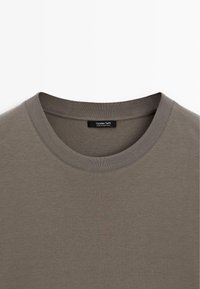 Gros plan sur un T-shirt marron à col rond avec un col côtelé et une étiquette Massimo Dutti à l'intérieur de l'encolure.