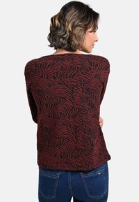 Roter und schwarzer Pullover mit einem strukturierten, abstrakten Muster. Lange Ärmel und lockere Passform, kombiniert mit blauen Jeans.