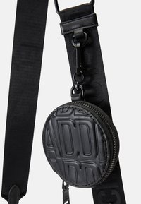 Mala circular preta feita de couro texturizado, com letras em relevo. Ligada a uma alça larga preta com um acabamento suave e acessórios de metal.