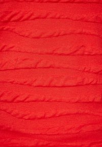 Červená tkanina s texturovaným povrchem, která má vyvýšené, vlnité pruhy, což vytváří vizuálně poutavý vzor. Měkký, elastický materiál.