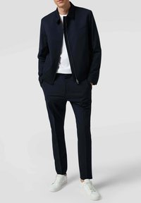 Giubbotto bomber blu navy con zip frontale, abbinato a pantaloni sartoriali blu navy e sneakers bianche. Tessuto liscio con un taglio moderno.