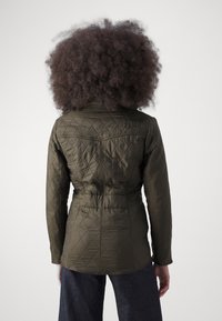 Olive green quilted jacket with diamond pattern, fitted waist, and long sleeves. Soft texture, front snap closure, and back yoke detail.