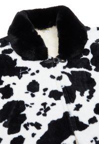Cappotto in pelliccia ecologica con stampa a macchie di mucca bianca e nera, caratterizzato da un colletto morbido, una superficie testurizzata e una chiusura con gancio nero.