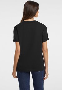 T-shirt nera con maniche corte arrotolate, scollatura rotonda e vestibilità comoda. Il tessuto sembra morbido con una finitura liscia.
